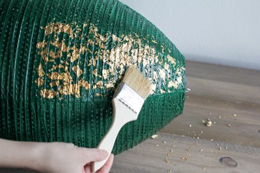 Hand with paint brush applying gold leaf on green lantern