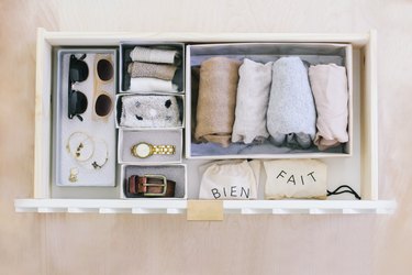 Wrapped sheets, ties, sunglasses, jewelry, and belt in variously sized hikidashi boxes in drawer against light wood background