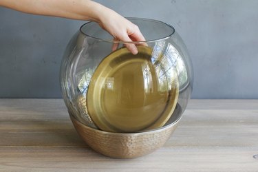 placing a gold-colored paper plate to create a floor on the bottom of a glass lamp globe