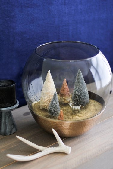 a holiday scene made from a glass lamp globe and bottle-brush trees