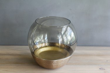 a glass lamp globe inside a copper bowl with a gold-colored paper plate at the bottom