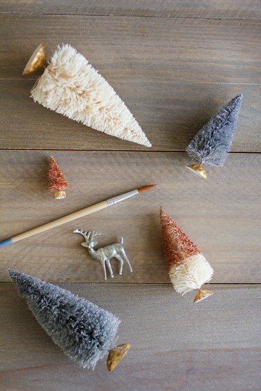 a paint brush, a deer figurine, and trees made from bottle brushes