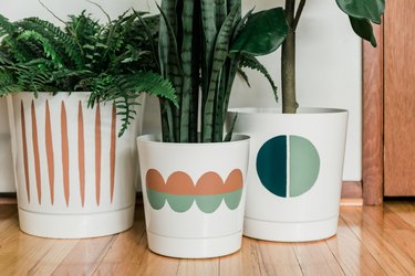 a trio of faux plants in white planters that have been painted with geometric designs