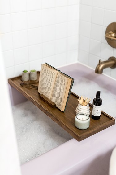 Wood bath tray with reading glasses, book, and plants over bathtub