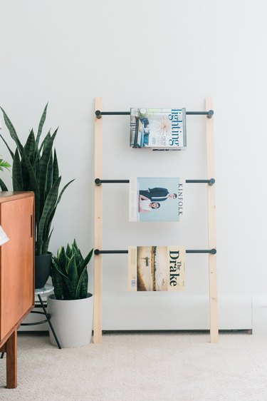 Wood and metal ladder with magazines next to potted plant and wood sideboard