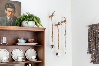 Clay bell wall hanging with wood china cabinet, plant, and art