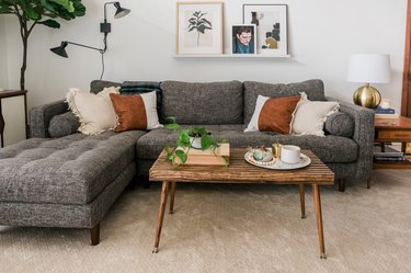 Midcentury-inspired wood slat coffee table with decorative book, potted plant, and plate with candles on tan carpet against grey couch in modern living room