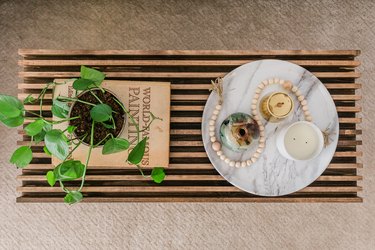 Midcentury-inspired wood slat coffee table with decorative book, potted plant, and plate with candles on tan carpet