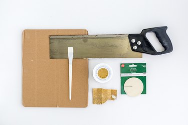 wooden disks, gold paint, a paint brush, a saw, sandpaper, and cardboard scrap