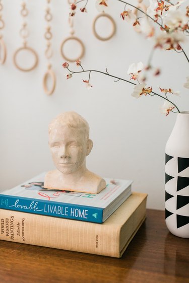 Portrait bust sculpture on books with geometric black-white vase with plant