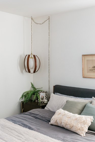 Bedroom with dark bedding, nightstand with plant, and vintage pendant lamp