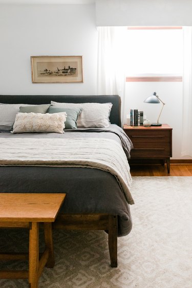 Bedroom with dark and light bedding on beige rug with night table and window