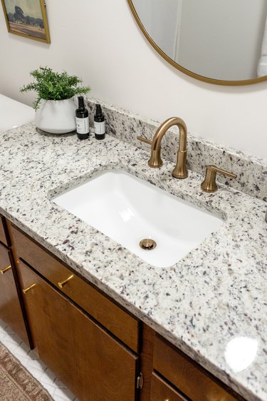 Bathroom sink with granite countertop and plant under mirror