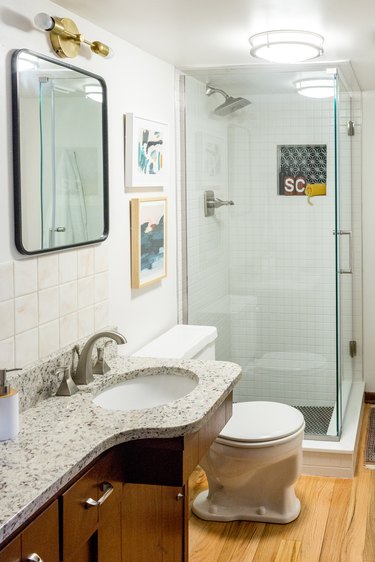 Bathroom with white wall tiles, granite vanity counter, hardwood floor, and glass door shower