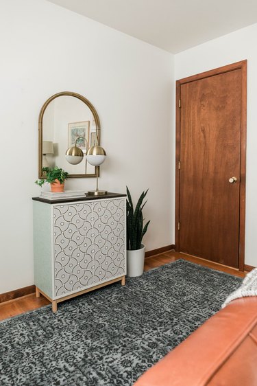 DIY entryway cabinet with plant, lamp, and books on hardwood floor with blue rug and plant against white wall with mirror