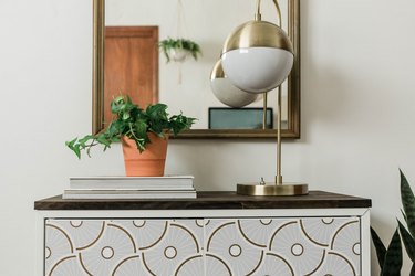 DIY entryway cabinet with plant, lamp, and books against white wall with mirror.