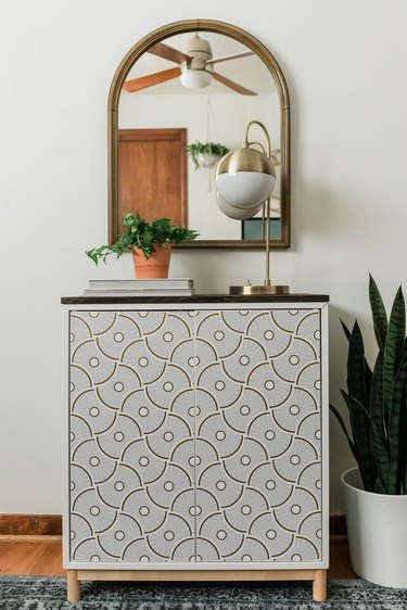 DIY entryway cabinet with plant, lamp, and books on hardwood floor with blue rug and plant against white wall with mirror