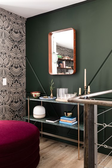 a corner of a room where a wall painted green meets one covered in an aztec-influenced silver pattern