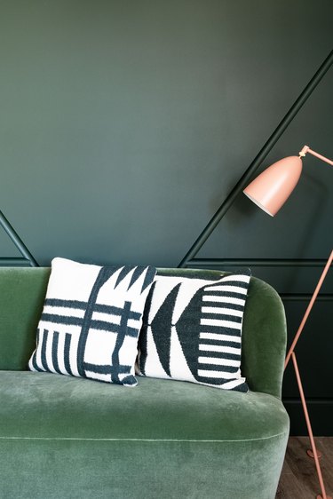 a medium-green couch against a dark green wall next to a pink floor lamp