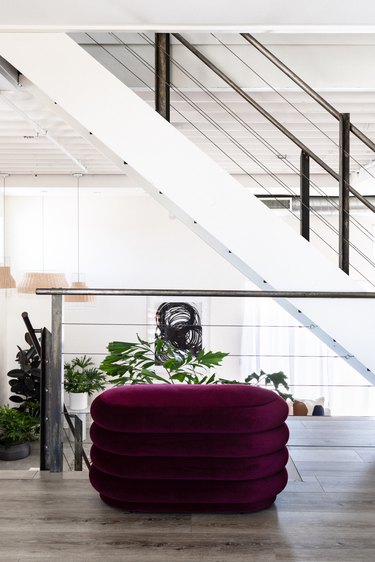 a large burgundy pouf under a white staircase