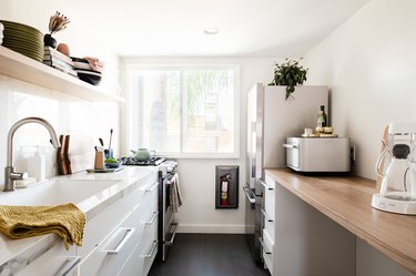 a small, narrow kitchen with white drawers below and open shelving above