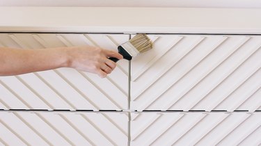 Hand using paint brush with white paint on IKEA wood dresser