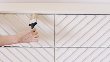 Hand using paintbrush to paint IKEA dresser with white paint