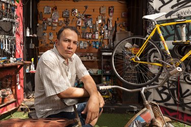 A person sitting in a workshop with bicycles and worship tools