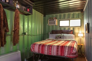 A bedroom with corrugated green metal walls, colorful bedding and retro furniture