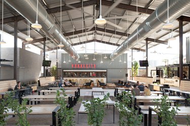 A bar in an industrial building with white pendant lights and wood tables