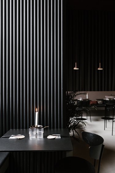 Minimalist bar with black dining furniture, pendant lights, and palm plants