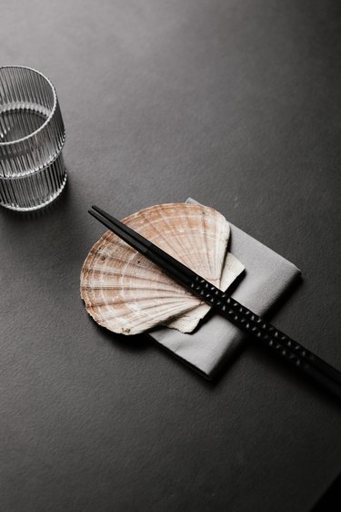 Black table with seashell supporting chopsticks next to glass