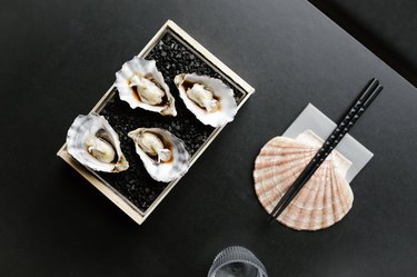 Black table with seashell supporting chopsticks with dish of oysters and a glass