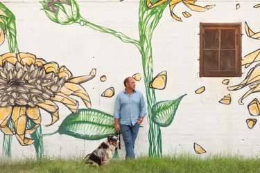 A person with a dog in front of a building wall with a painted sunflower mural
