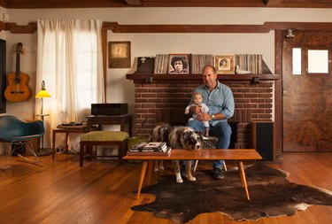 A person sitting with a baby in a mid-century living room with wood floors and brick fireplace