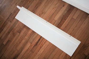 Long white angled board resting on wood flooring