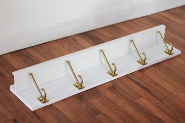 White kitchen wall hangers with gold hooks resting on wooden floor