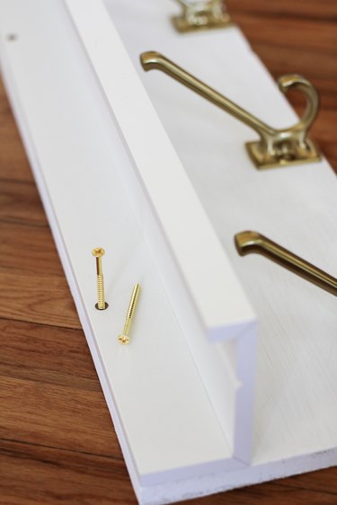 White kitchen wall hangers with gold hooks resting on wood flooring next to gold screws