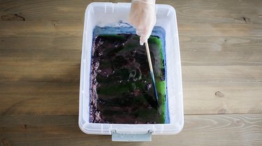 Hand using paint stick to stir indigo dye in bucket