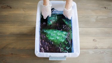 Gloved hands submerging stocking in bucket with indigo dye