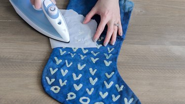 Hands using iron and wax paper for wax design on a blue indigo stocking