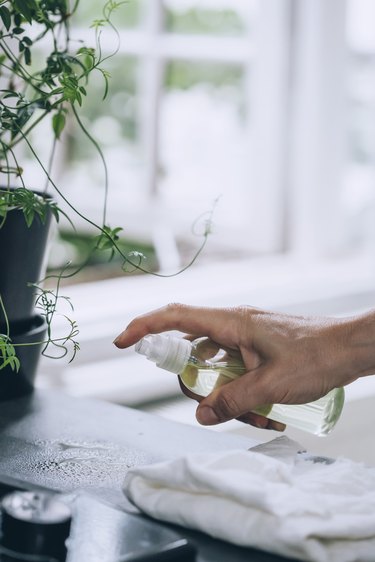 using a spray bottle full of lemon-vinegar solution to clean a countertop