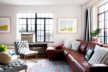 A living room with a leather sectional couch, two gray upholstered chairs, and a colorful pastel rug.
