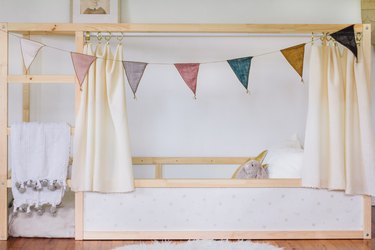 a kura bed frame that has been hacked by adding curtains and bunting and decorating surfaces with wallpaper