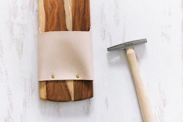 a tack hammer and a cutting board with leather strips attached with tacks
