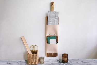 a wall-mounted letter holder made from a cutting board and leather strips