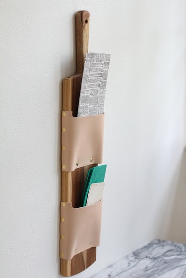 a wall-mounted letter holder made from a cutting board and leather strips
