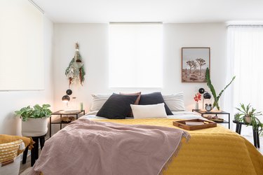 White walled bedroom with plants and a bed with beige-yellow-black bedding