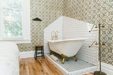 a claw-foot tub sits in a corner of a bathroom on a slightly  raised penny tile platform