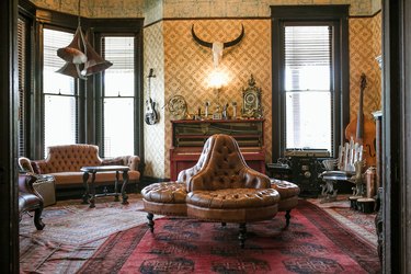 a sitting room with clubby overstuffed leather furniture as well as moorish influenced deco wall art and a cow skull